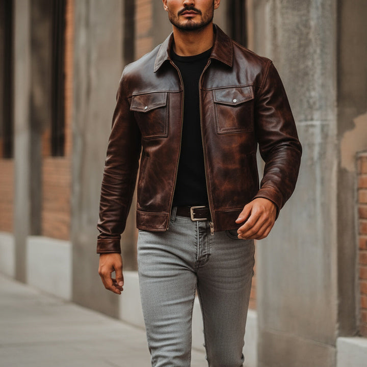 Man wearing a brown leather jacket and gray jeans standing in an urban setting.