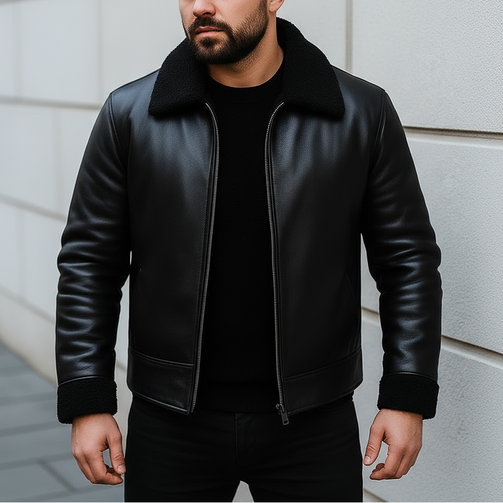 Man wearing a black leather jacket against a light gray wall.