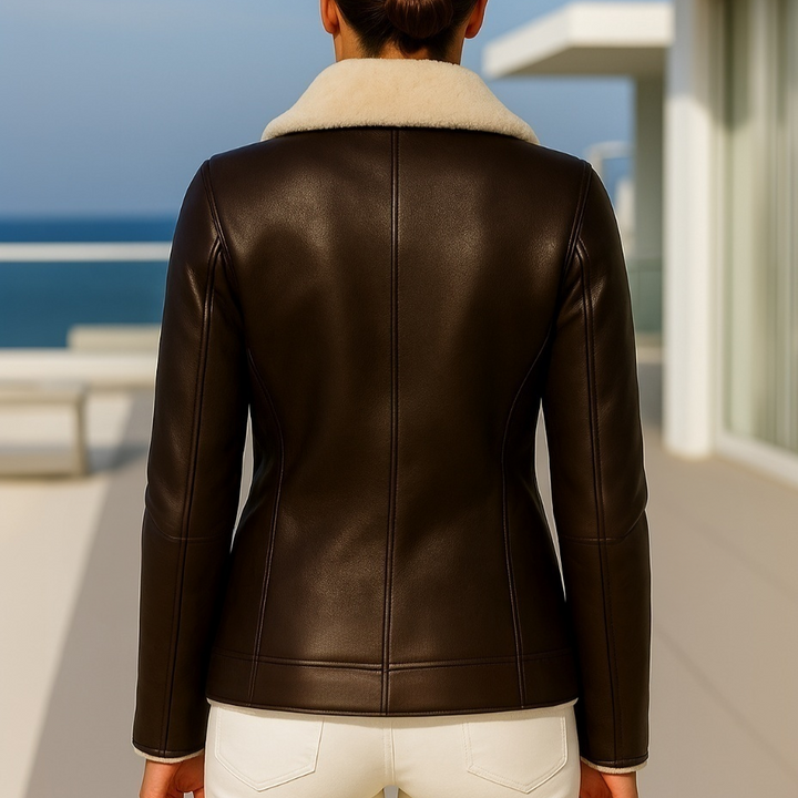 Person wearing a brown leather jacket with a white interior lining, standing on a balcony with ocean view.